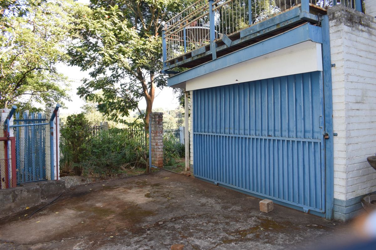 Rear exterior view showing a concrete driveway, a metal garage door, and an elevated balcony with weathered metal railings.