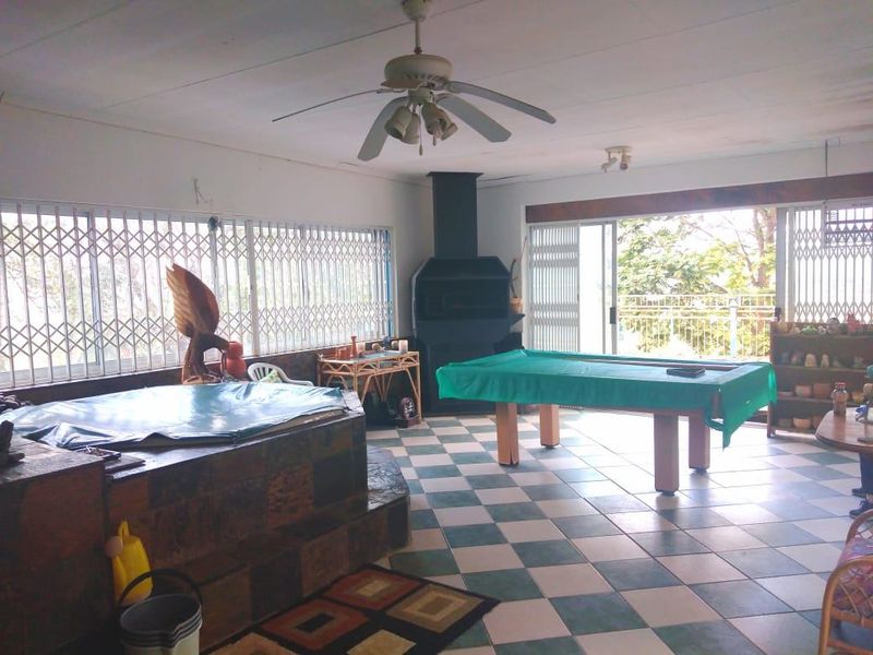 Spacious living area featuring a built-in fireplace, tiled flooring, ceiling fan, and large sliding doors with security gates leading to the outdoors.