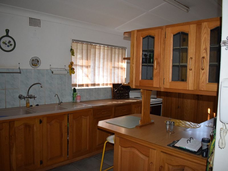 A functional kitchen featuring timber cabinetry, laminate countertops, a double bowl sink, and a breakfast bar, offering potential for modern updates.