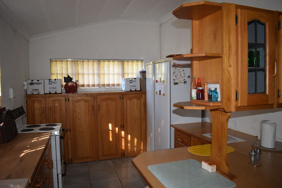 A functional kitchen featuring timber cabinetry, tiled flooring, and an electric stove, offering a dated aesthetic with potential for modern renovation.