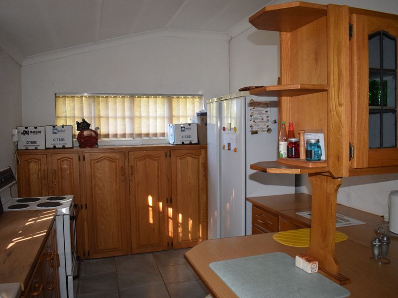A functional kitchen featuring timber cabinetry, tiled flooring, and an electric stove, offering a dated aesthetic with potential for modern renovation.