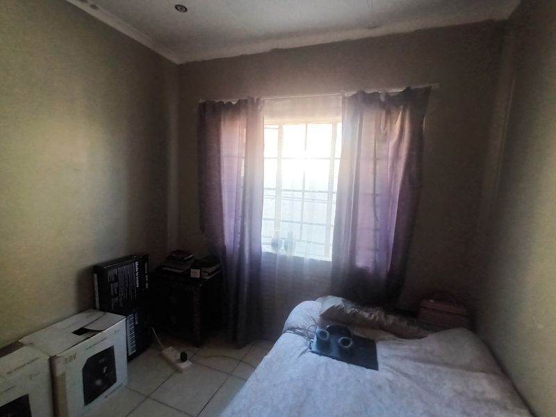 A standard bedroom featuring tiled flooring, recessed ceiling lighting, and a window fitted with security burglar bars.