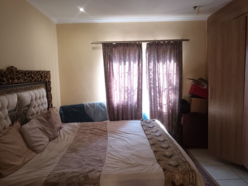 A bedroom featuring a built-in wardrobe, tiled flooring, and a window with curtain rod, providing a functional space for rest.