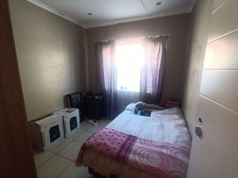 A compact bedroom featuring tiled flooring and recessed ceiling lighting, requiring cosmetic updates to the walls and finishes.