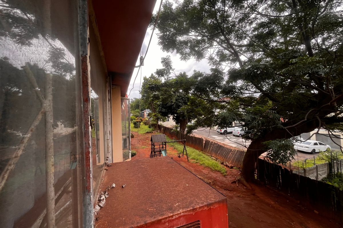 Exterior view of the property rear showing significant weathering, corrosion on metal window frames, and a rusted concrete ledge requiring maintenance.