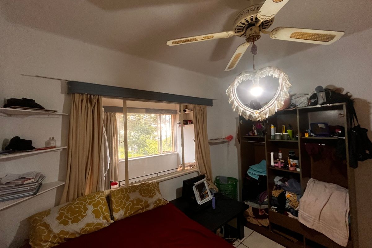 A bedroom featuring tiled flooring, a ceiling fan, and built-in shelving, with a window providing natural light and views of the exterior.