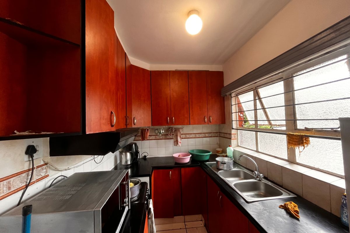 A functional kitchen featuring dark laminate cabinetry, a double bowl stainless steel sink, tiled backsplash, and a window with security bars.