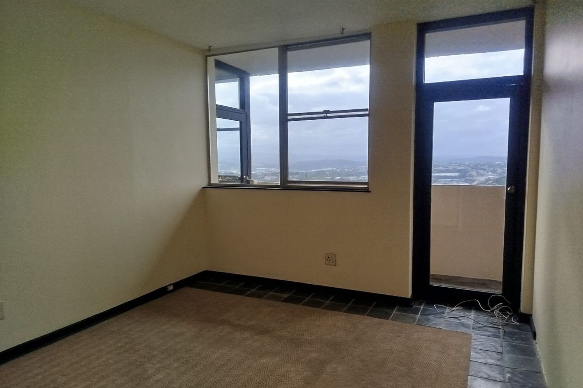 An empty bedroom featuring a mix of carpet and tile flooring, with large windows and a glass door providing access to a balcony with views.