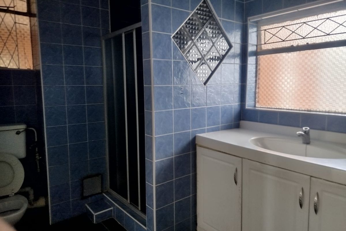A dated bathroom featuring blue wall tiles, a vanity cabinet with integrated sink, a shower enclosure, and a toilet.