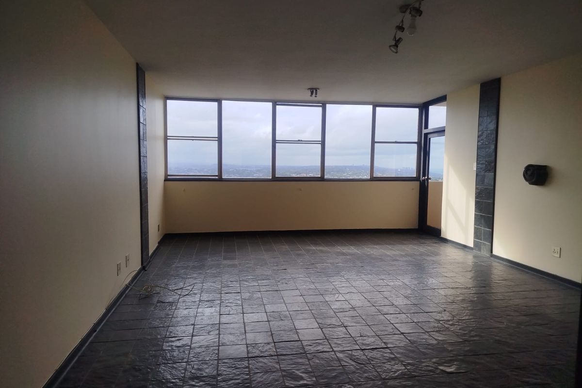 Spacious, empty living area featuring dark tiled flooring, decorative stone wall accents, and large windows offering expansive elevated views.