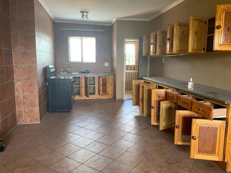 A spacious, empty kitchen featuring wooden cabinetry, tiled flooring, and a freestanding stove, offering a functional layout ready for modernization.
