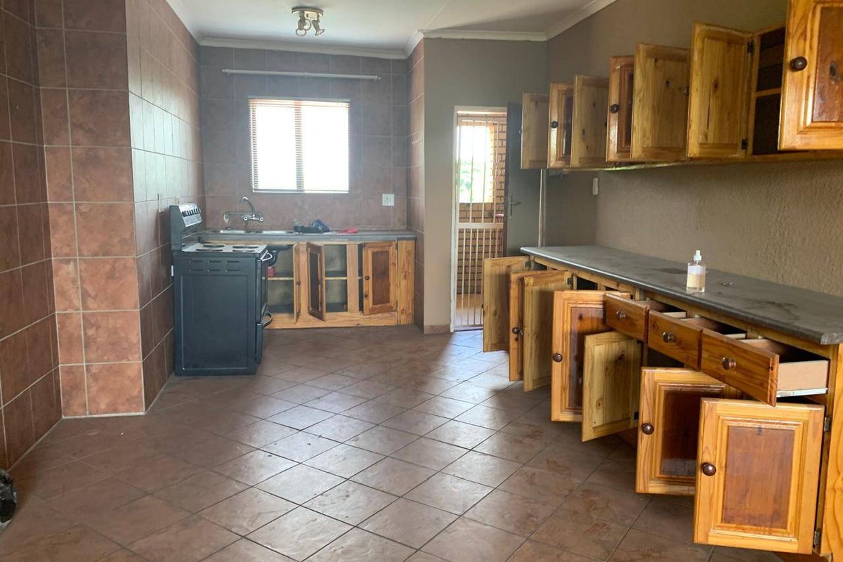 A spacious, empty kitchen featuring wooden cabinetry, tiled flooring, and a freestanding stove, offering a functional layout ready for modernization.