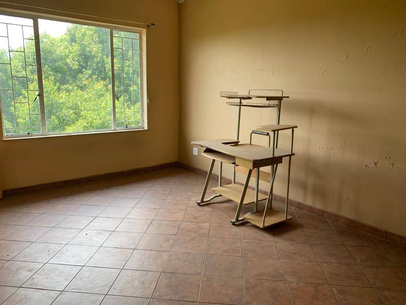 A vacant bedroom featuring tiled flooring and a large window with security bars, requiring cosmetic updates to the wall finishes.