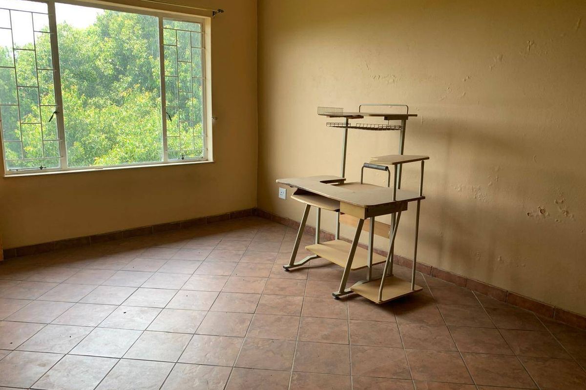 A vacant bedroom featuring tiled flooring and a large window with security bars, requiring cosmetic updates to the wall finishes.