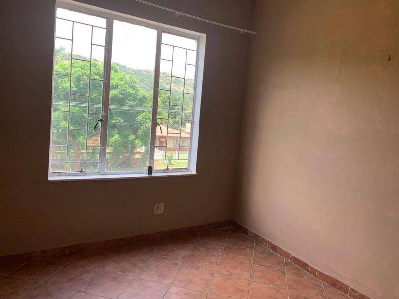 An empty bedroom featuring tiled flooring, security bars on the window, and neutral wall finishes, offering a blank canvas for personalization.