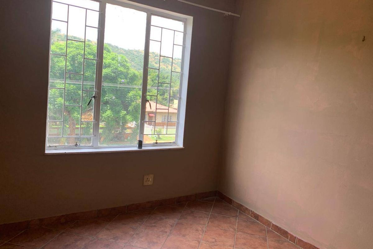 An empty bedroom featuring tiled flooring, security bars on the window, and neutral wall finishes, offering a blank canvas for personalization.