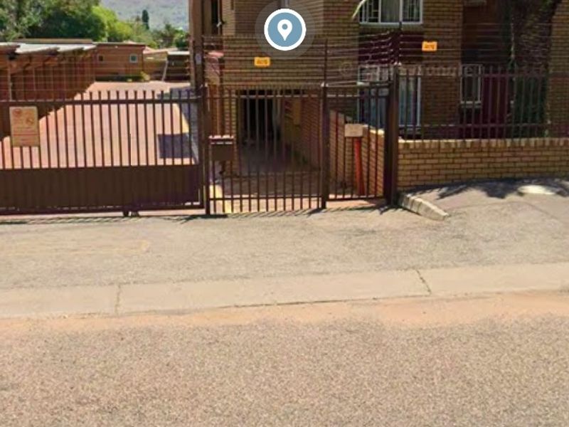 Street view of the apartment complex entrance featuring brick facade, secure gated access, and perimeter electric fencing.