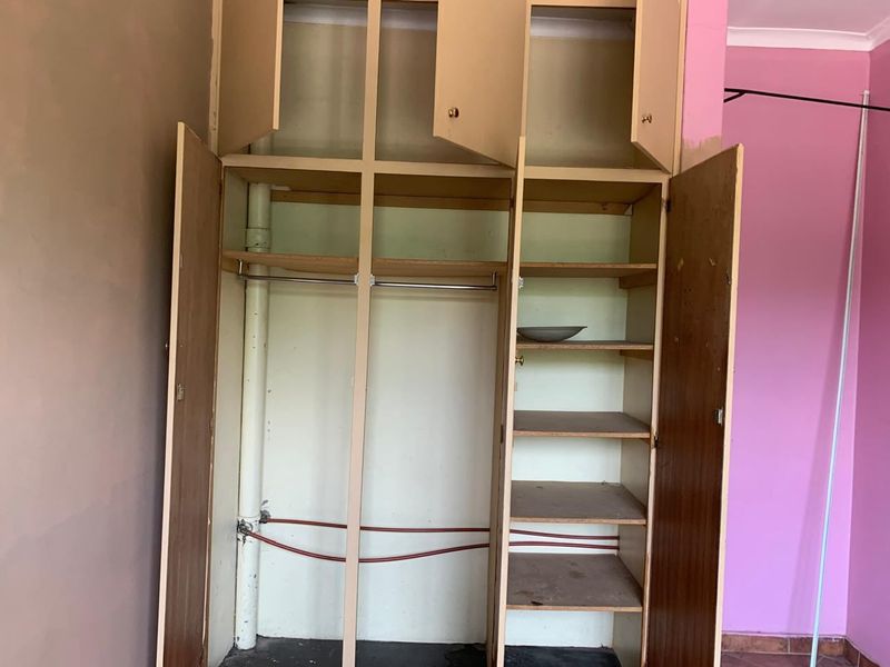 A bedroom featuring a built-in wardrobe with exposed plumbing and electrical wiring, requiring cosmetic updates and repairs to the cabinetry and wall finishes.