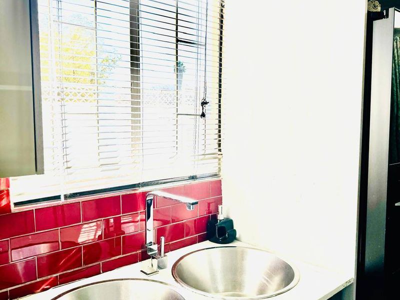 A functional scullery area featuring a double stainless steel sink, chrome mixer tap, and striking red subway tile backsplash with overhead storage.