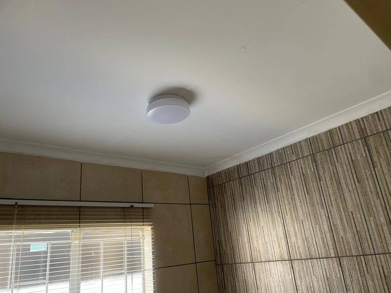 A close-up view of a bathroom ceiling featuring a mounted light fixture and decorative ceramic wall tiling.