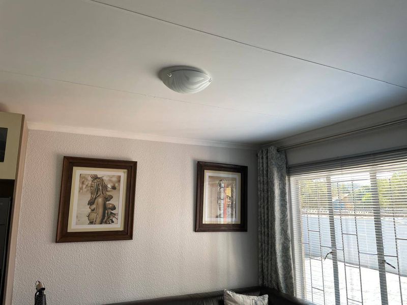A living room interior featuring textured walls, a ceiling-mounted light fixture, and window treatments including venetian blinds and curtains.