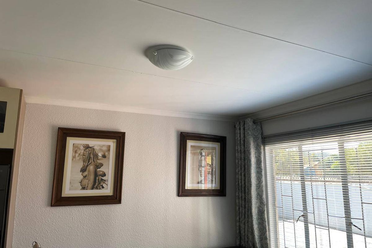 A living room interior featuring textured walls, a ceiling-mounted light fixture, and window treatments including venetian blinds and curtains.