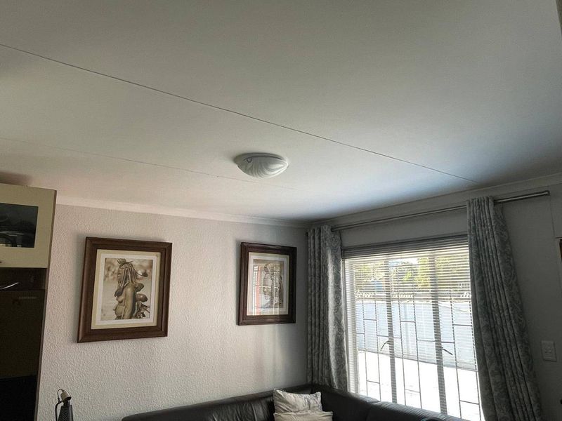 A living room area featuring a ceiling light fixture, window with security bars, and venetian blinds.