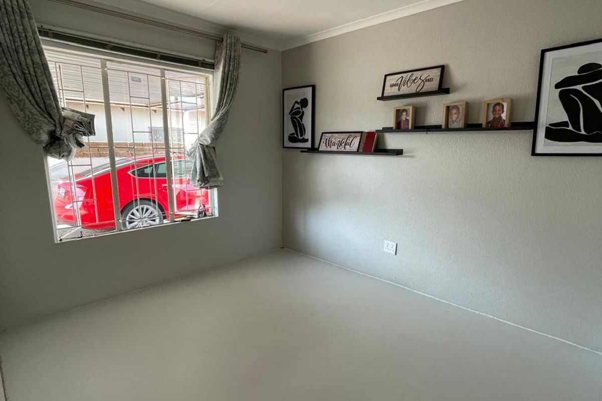 A clean, empty bedroom featuring neutral walls, a window with security bars, and installed curtain rails, providing a blank canvas for personalization.