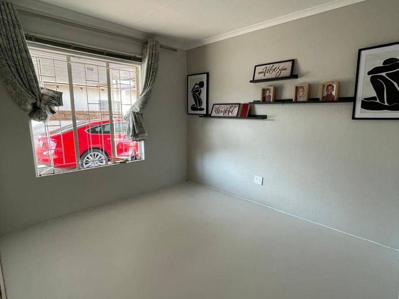A clean, empty bedroom featuring neutral walls, a window with security bars, and installed curtain rails, providing a blank canvas for personalization.