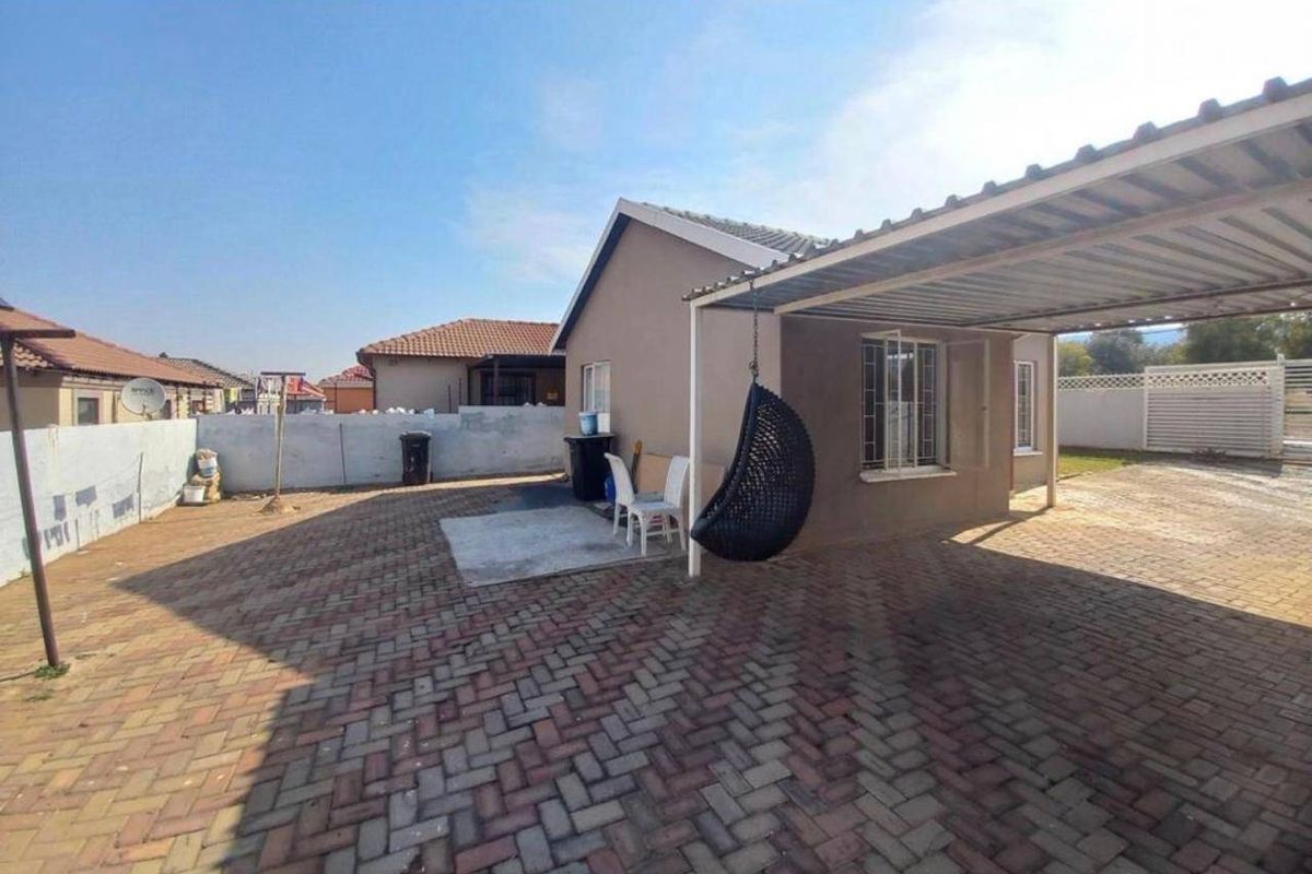 Rear exterior view of the property featuring a paved driveway, a covered carport, and a perimeter wall.