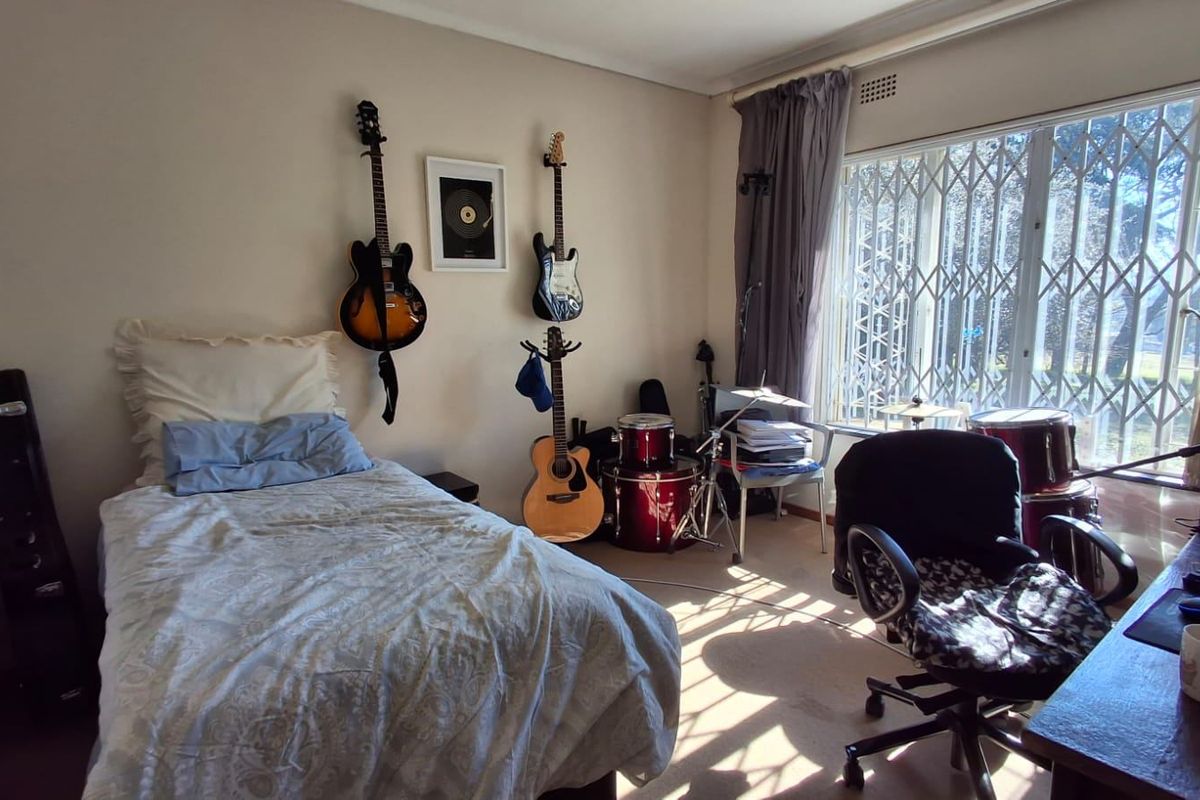 A functional bedroom featuring a built-in cupboard, large window with security gate, and neutral wall finishes.