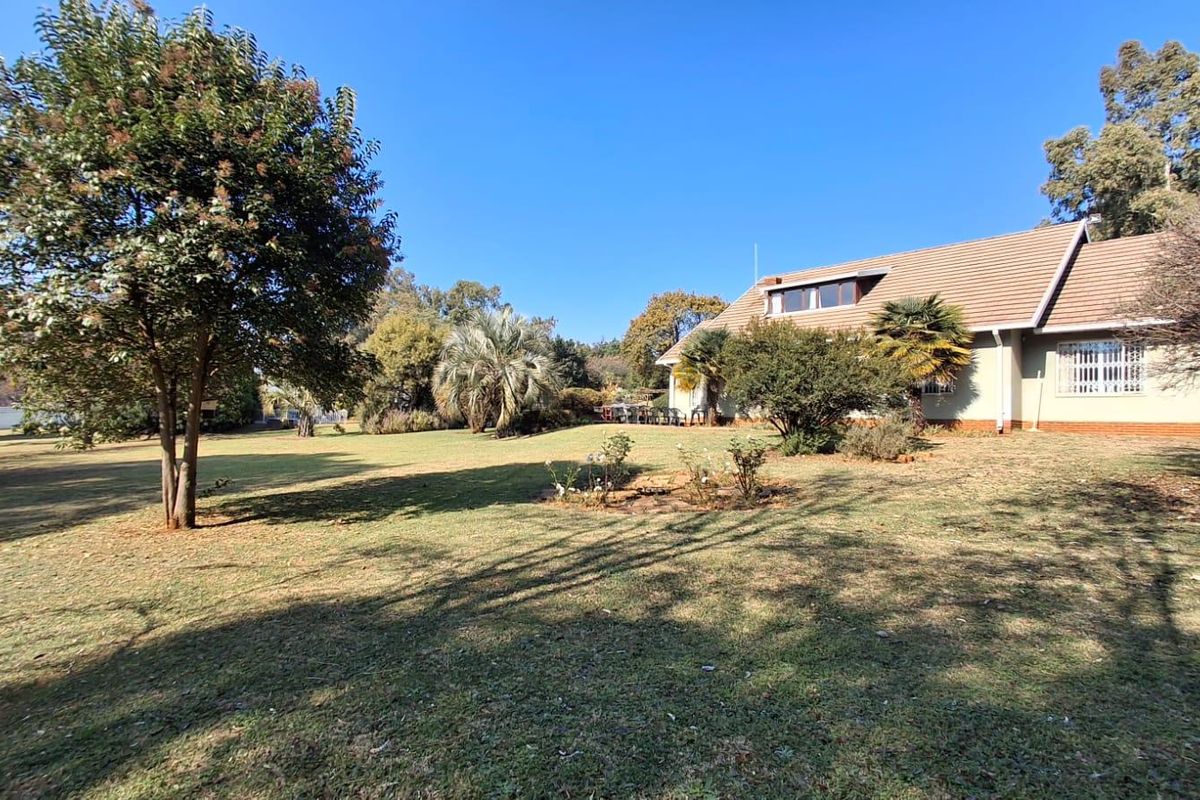 A spacious rear garden view featuring a large lawn, mature trees, and the rear elevation of the house with a tiled roof.