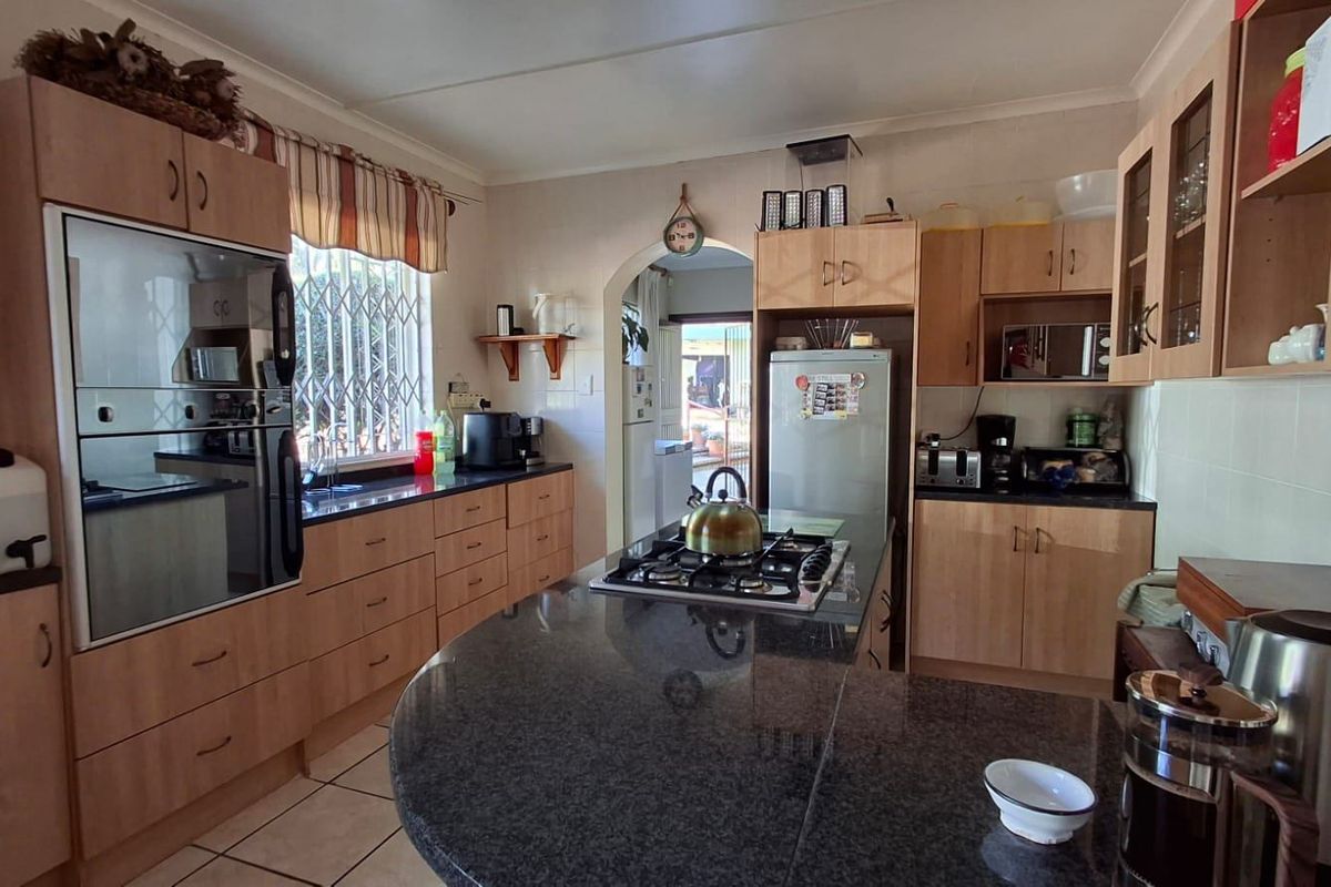 A functional kitchen featuring light wood cabinetry, dark granite countertops, a built-in oven, and a central island with a gas hob.