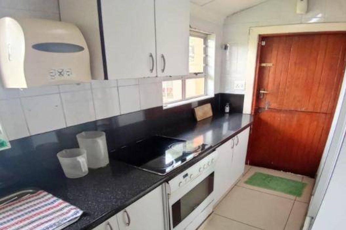 A functional kitchen featuring dark countertops, built-in oven and hob, white cabinetry, and a solid timber door leading to the exterior.