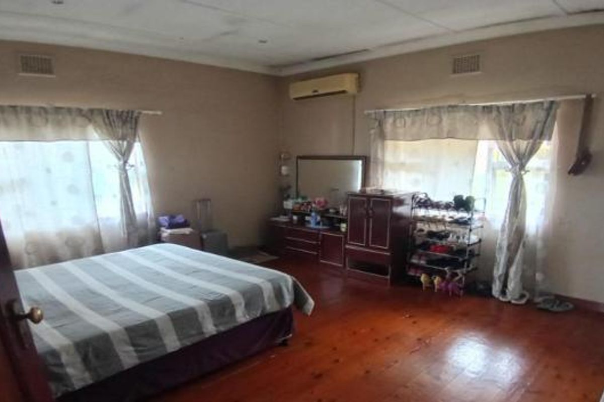Spacious bedroom featuring timber flooring, an air conditioning unit, and dual windows, offering a functional layout ready for cosmetic updates.