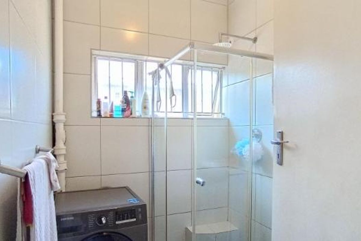 A functional bathroom featuring a glass shower enclosure, full-height wall tiling, and a window with security bars.