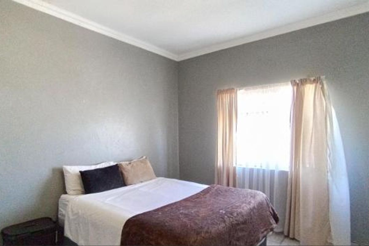 A simple bedroom featuring neutral grey walls, crown molding, and a window with curtains.