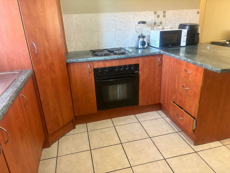 A functional kitchen featuring wood-look laminate cabinetry, dark countertops, ceramic tile flooring, and a built-in oven with an electric hob.