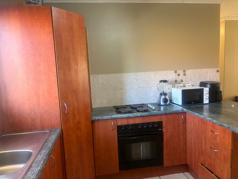 A functional kitchen featuring wood-finish cabinetry, laminate countertops, a built-in oven with electric hob, and a tiled backsplash.
