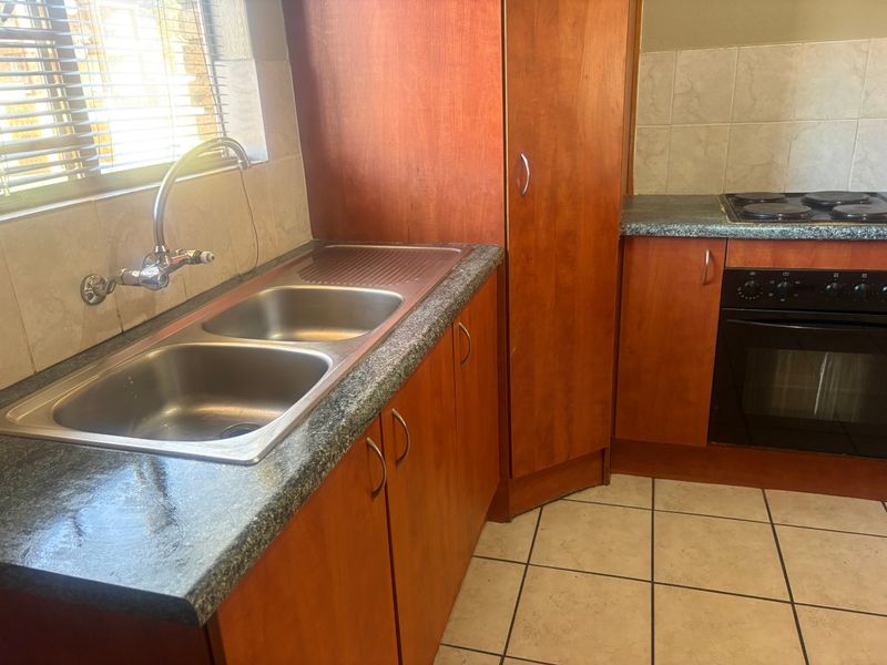 A functional kitchen featuring wooden cabinetry, a double bowl stainless steel sink, built-in oven, electric hob, and tiled flooring.