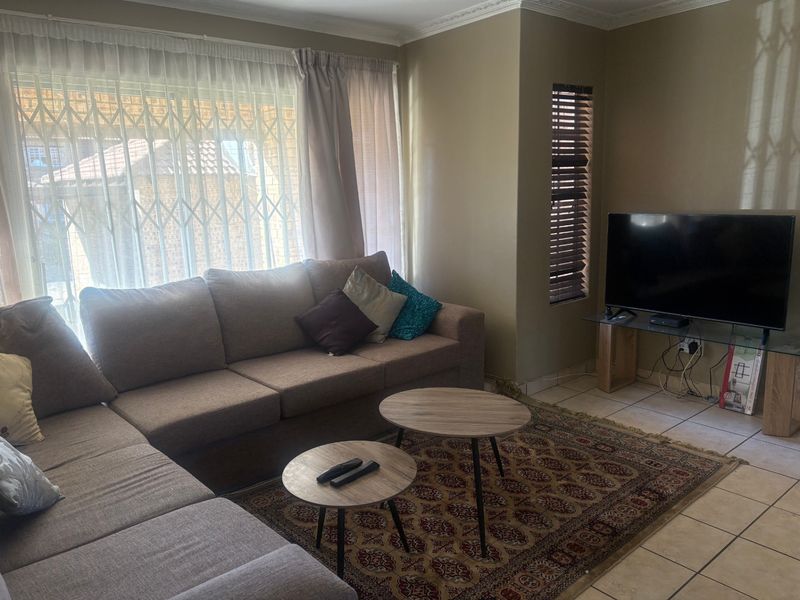 A comfortable living room featuring ceramic floor tiles, decorative cornice, and natural light through large windows fitted with security gates and blinds.