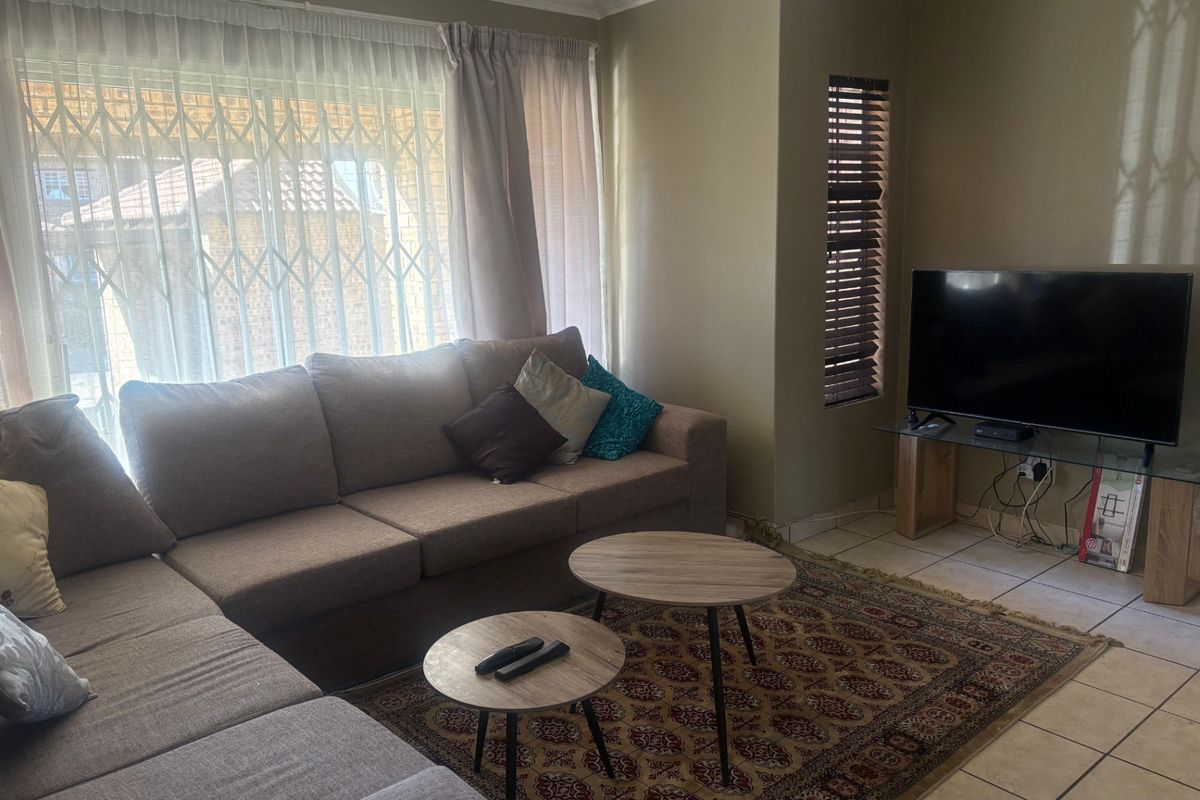 A comfortable living room featuring ceramic floor tiles, decorative cornice, and natural light through large windows fitted with security gates and blinds.
