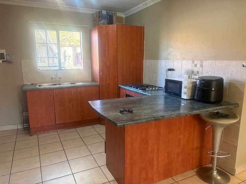 A functional kitchen featuring laminate cabinetry, dark countertops, a double bowl sink, built-in hob, and tiled flooring with a neutral backsplash.