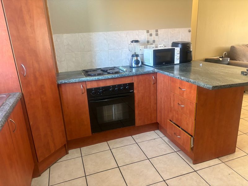 A compact kitchen featuring wooden cabinetry, a built-in oven with electric hob, tiled splashback, and durable ceramic floor tiles.