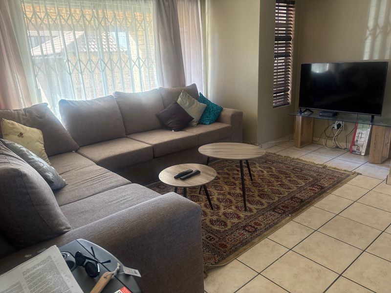 A comfortable living room featuring tiled flooring, large windows with security gates, and venetian blinds, providing a functional and well-lit space.