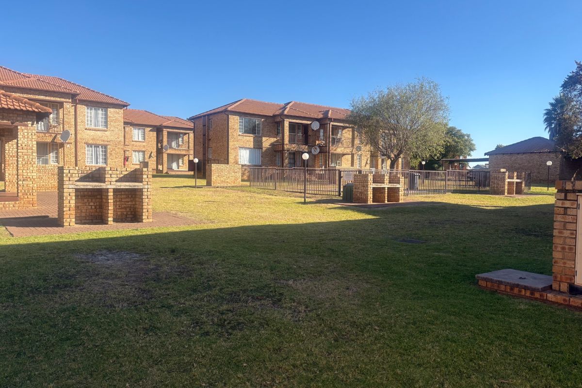 A well-maintained communal garden area featuring brick-built braai facilities, paved pathways, and established lawns between apartment blocks.
