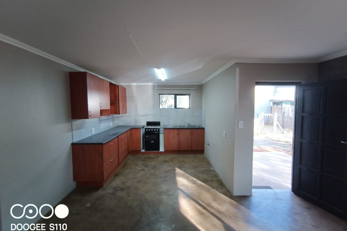A functional kitchen featuring wood-tone cabinetry, dark countertops, and a freestanding stove, with direct access to the exterior.