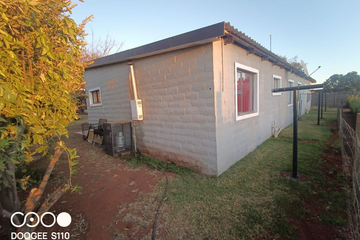 Rear view of the farm dwelling featuring concrete block construction, a corrugated metal roof, and an external gas geyser installation.