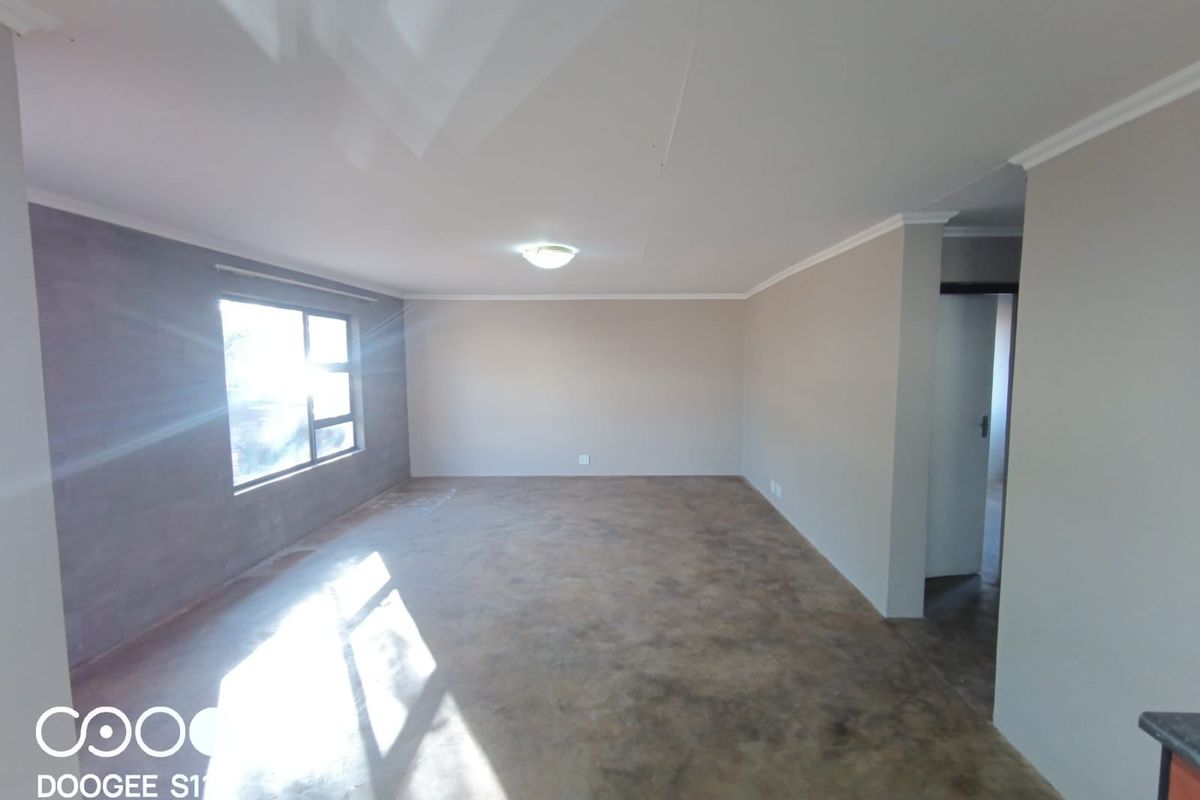 An empty, open-plan living area featuring neutral wall tones, a large window, and a concrete floor finish.