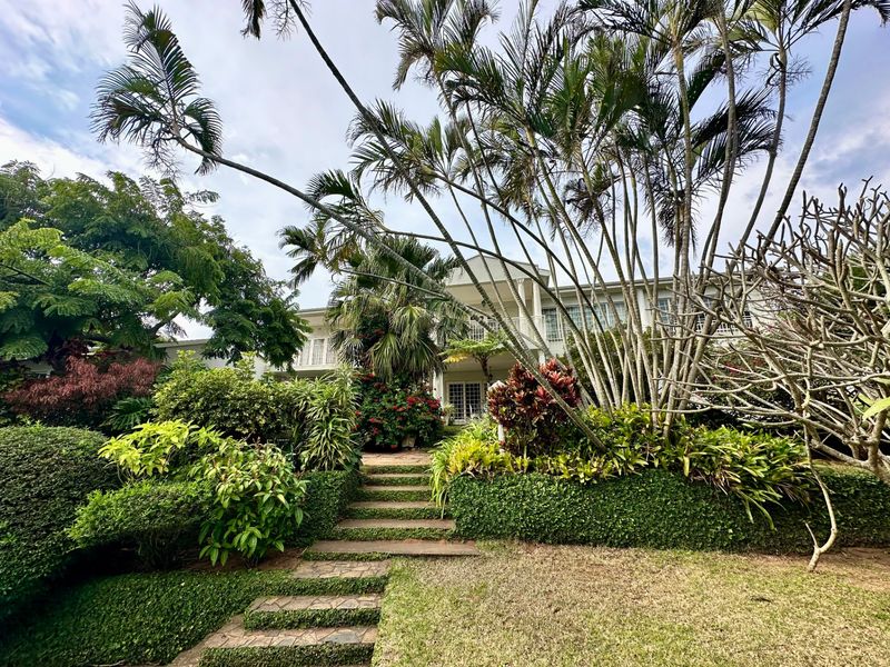 A lush, landscaped rear garden featuring stone steps leading up to a two-story residence with a balcony and french doors.